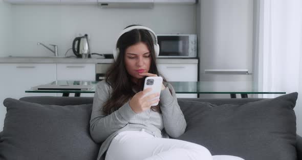 A Shocked Brunette Girl in a Grey Sweater Saying Yes Looking Smartphone and Covering Her Mouth While