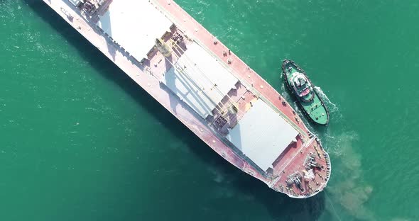 Large cargo ship enters the port escorted by tugboats.