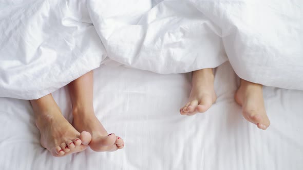 Mother and Child Lie on Bed with White Sheets Feet Side By Side in Comfortable Bed at Home