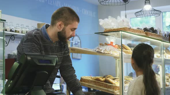 Young Male Baker Working at His Store Helping Little Girl Choosing Desserts