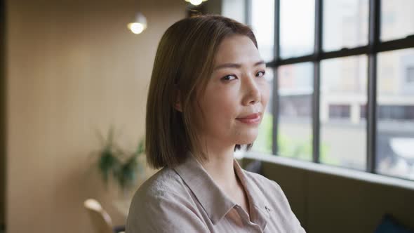 Asian businesswoman standing looking out of window in modern office