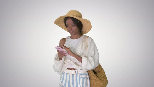 Smiling Young African American Woman in a Straw Hat Texting on Her Phone on Gradient Background