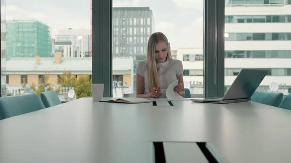 Young Business Woman in Conference Room with Papers. Elegant Blond Woman Sitting at Long Table in