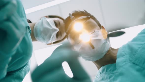 Surgeon with Nurse Are Looking Down at Camera. Handsome Young Doctor in Surgical Mask Is Holding