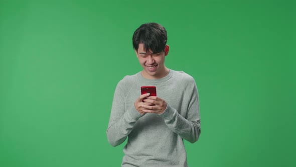 An Asian Man Enjoy Using Mobile Phone While Standing On Green Screen In The Studio