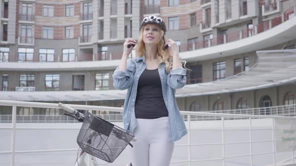 Portrait Pretty Blond Woman Putting a Bike Helmet on Her Head and Riding Her Bicycle Against the