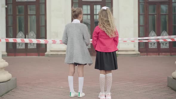 Wide Shot of Two Girls Standing in Front of Closed School During Coronavirus Lockdown. Sad
