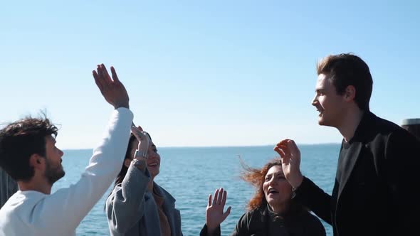 Slow motion shot of smiling friends high fiving at seafront