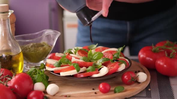 Pouring Balsamic Sauce on Caprese Salad with Cherry Tomatoes and Mozzarella Cheese Balls