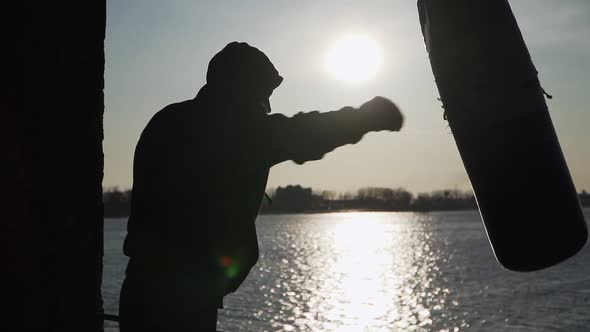 Boxer beats punching bag on sunset background. Silhouette motivation sport boxing. Slow motion