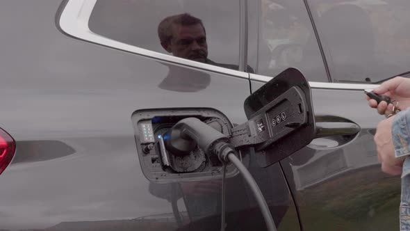 Close up view of man unplugging charging cable to charging station for electric car.