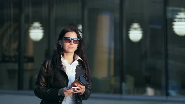 Young Attractive Businesswoman with Cup of Coffee Walking with Smart Phone in the City with Office