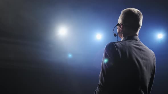 Rear View of Men Speaking Through a Microphone in Dark Conference Hall. Man Talks Into Microphones