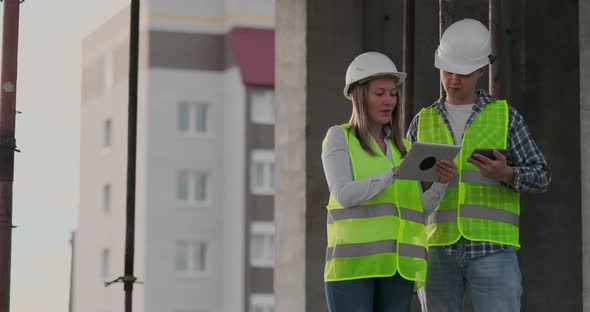 Construction Worker Man and Architect Woman in a Helmet Discuss the Plan of Construction of House