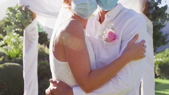 Portrait of happy caucasian newly wed couple touching heads at altar, wearing face masks