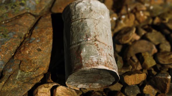 Rusty Destroyed Metal Barrel on Beach Rocks