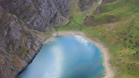 Flying and Landing a Mountain Lake with Turquoise Water and Green Grass. Reflection Sky and Clouds