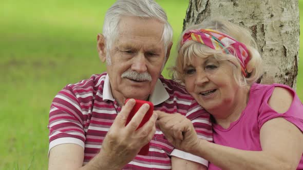 Family Picnic. Senior Old Grandparents Couple in Park Using Smartphone Online Browsing, Shopping