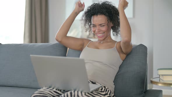 Excited African Woman Celebrating Success on Laptop at Home