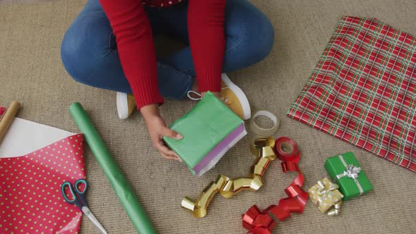 African american plus size woman wearing santa hat, packing presents in living room at christmas