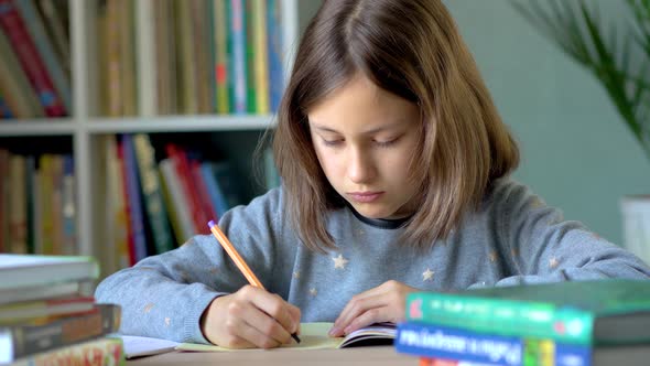 A Girl Sits at a Table and Writes in a Notebook