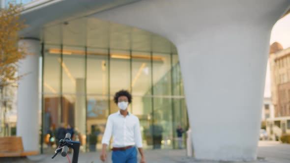 Portrait of Afro American Businessman in Mask Leaving Business Center and Riding Away on Scooter