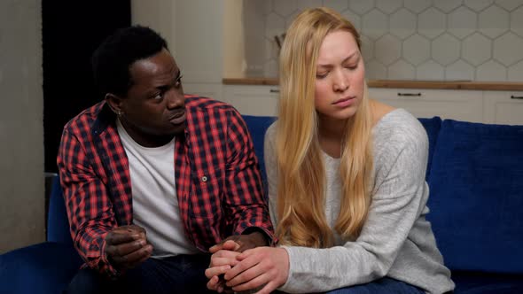 African American Man Calms Caucasian Upset Woman Sitting on Couch at Home