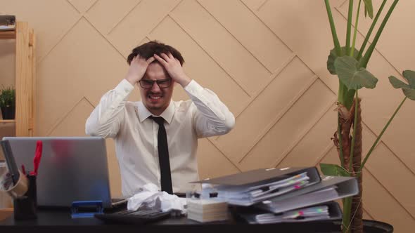 Office worker with tousled hair writes in notebook and irritably tears out piece of paper, crumples