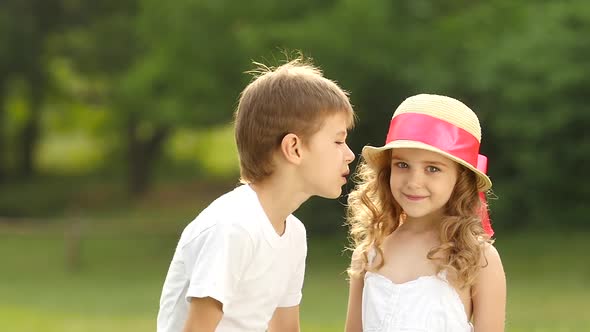 Little Boy Kisses the Girl on the Cheek, She Is Embarrassed and Smiles. Slow Motion