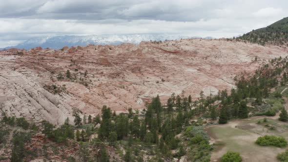 Slow rise with drone over rocky crest to reveal open landscape and snowy mountains in the distance