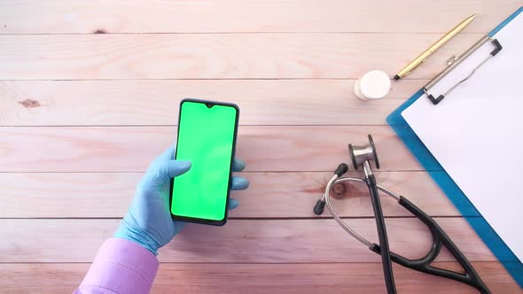 Top View of Hand in Latex Gloves Holding Smart Phone on Clinic Table