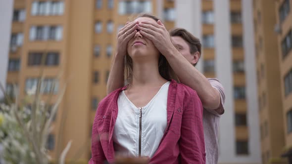 Young Beautiful Wife Standing at New House with Husband Covering Eyes with Hands