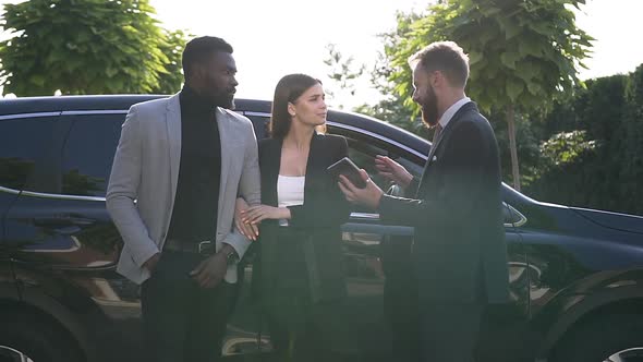 Salesman Presenting a New Car to Young Couple in Outdoors