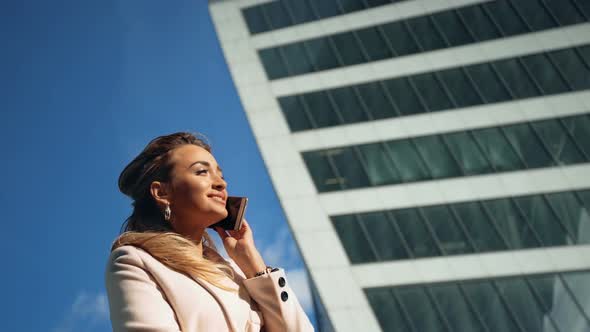 Beautiful Young Business Woman Calling By Phone on the Background of Skyscrapers