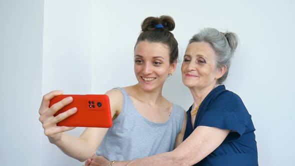 Adult Daughter and Senior Mum are Taking Selfportrait Picture Selfie on Red Smartphone Together