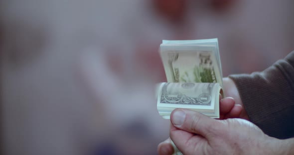 Slow motion medium shot of a person holding a bundle of prop money as they flip through the bills.