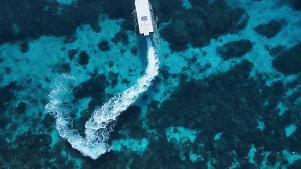 Unique view of a dive boat as it maneuvers through the water over a tropical reef system. High drone