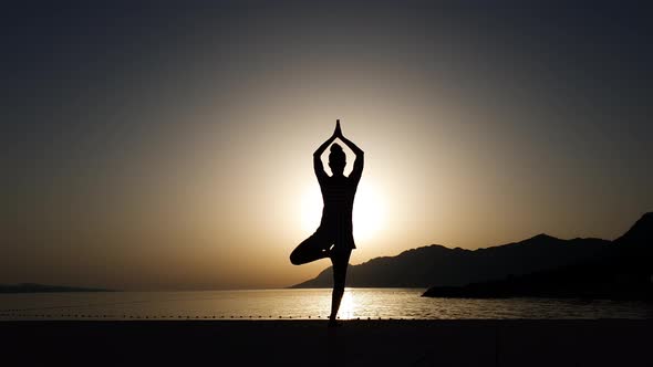 Silhouette of woman practicing yoga at sunset by the sea