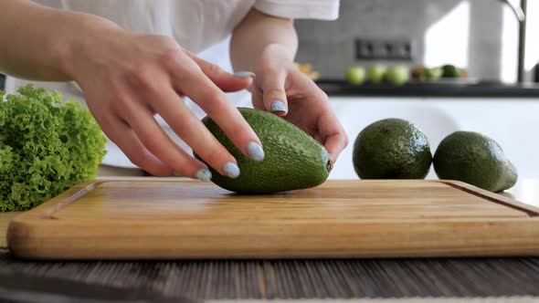 Female Hands Show a Cut Avocado in 2 Parts