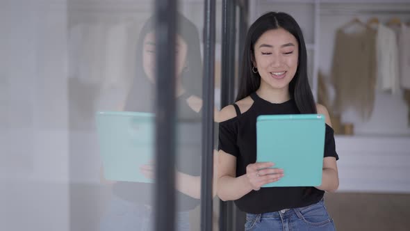 Confident Smart Young Asian Woman Talking at Tablet Virtual Conference Standing in Bedroom with