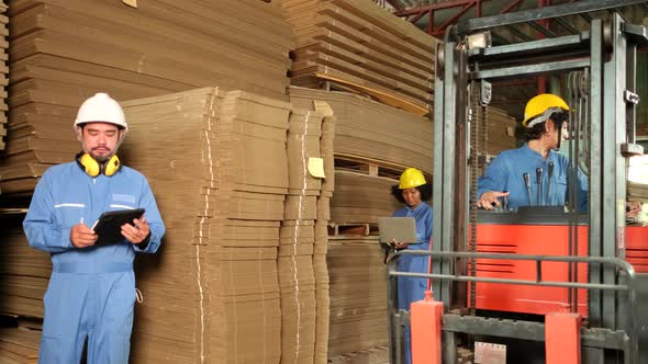 Workers team inspect stock at factory warehouse, management piles of  cardboard.