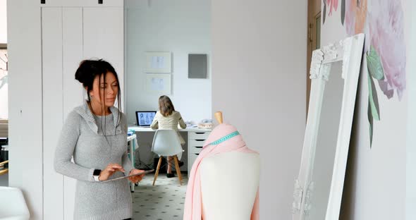 Fashion designer using tablet and examining the fabric on dressmakers model