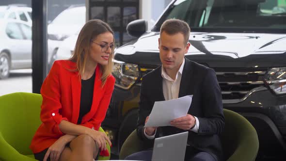 Seller and Buyer Are Studying the Contract of Sale of the Car. Beautiful Woman Buys a Car