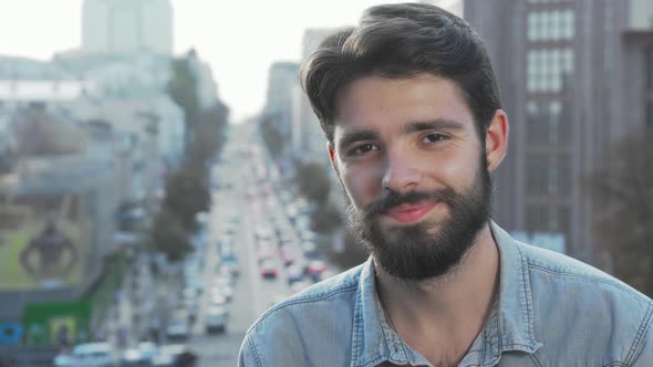 Young Bearded Man Smiling To the Camera with City on Background