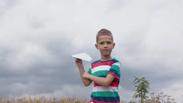 Happy Little Boy Playing With A Paper Airplane In A Field.