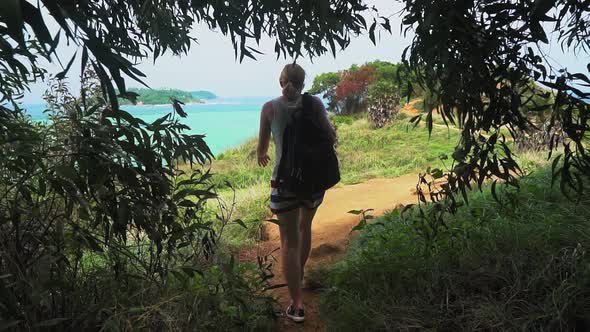 Back view of woman with backpack hiking in tropical island mountains