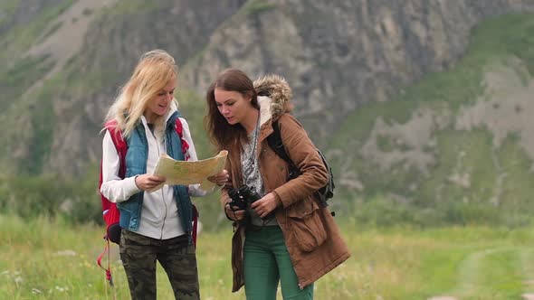 Young Women Travel in the Mountains. Using the Map and Binoculars. Two Friends Travel Together. Two