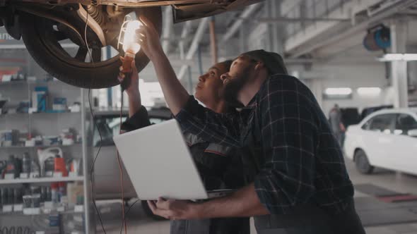 Two Auto Mechanics with Laptop Inspecting Car