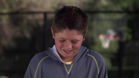 Boy at park smiling then glancing down.