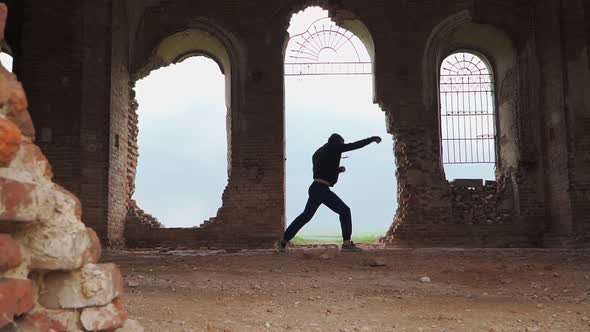 Man boxer in the hood trains beats in an abandoned building. Shadow Boxing. Outdoor workout.